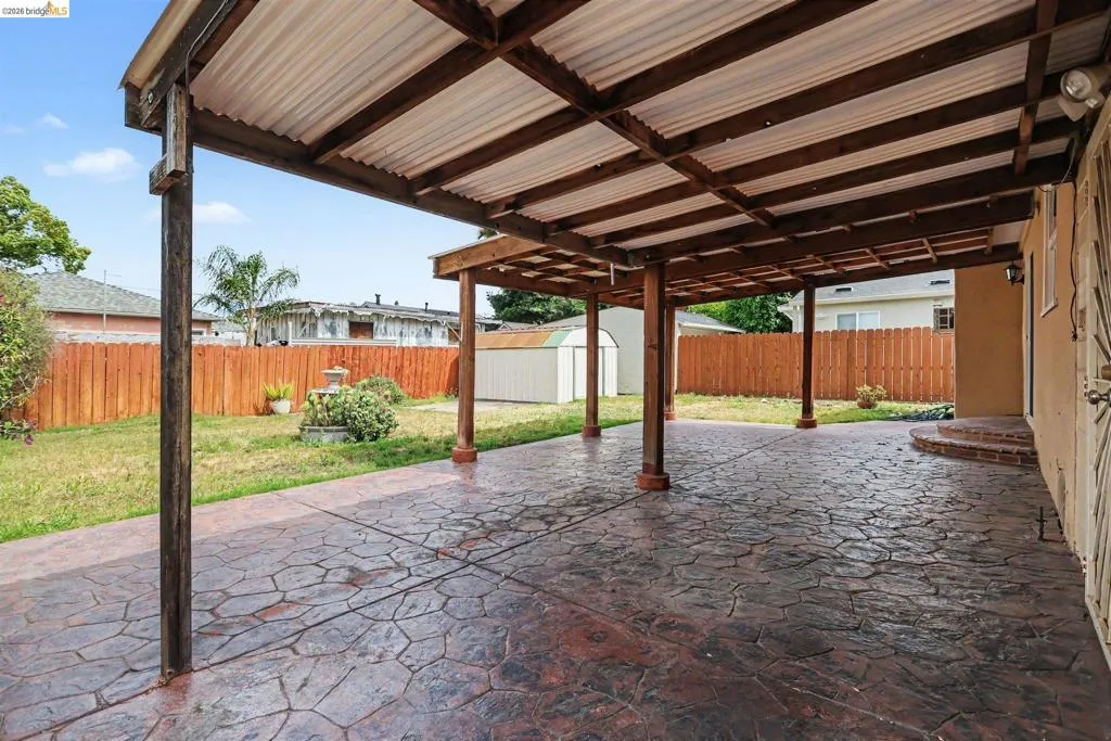 Expansive covered patio featuring stamped concrete flooring, exposed wood beams, and a corrugated roof