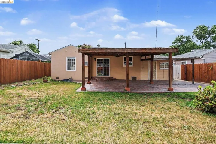 Backyard featuring a covered patio with a stamped concrete surface, a stucco exterior, sliding glass doors, and a wood privacy fence