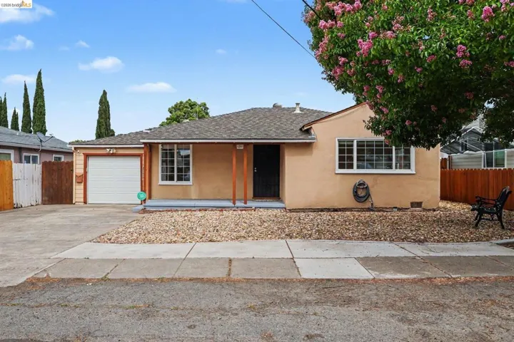 Stucco-finish exterior with a covered entry, attached garage, front landscaping with gravel, and a concrete driveway
