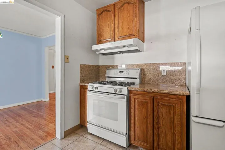 Kitchen featuring wood cabinetry, a white gas range with overhead ventilation, and a white refrigerator