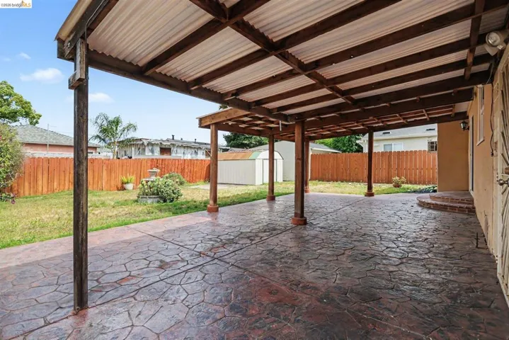 Expansive covered patio featuring stamped concrete flooring, exposed wood beams, and a corrugated roof