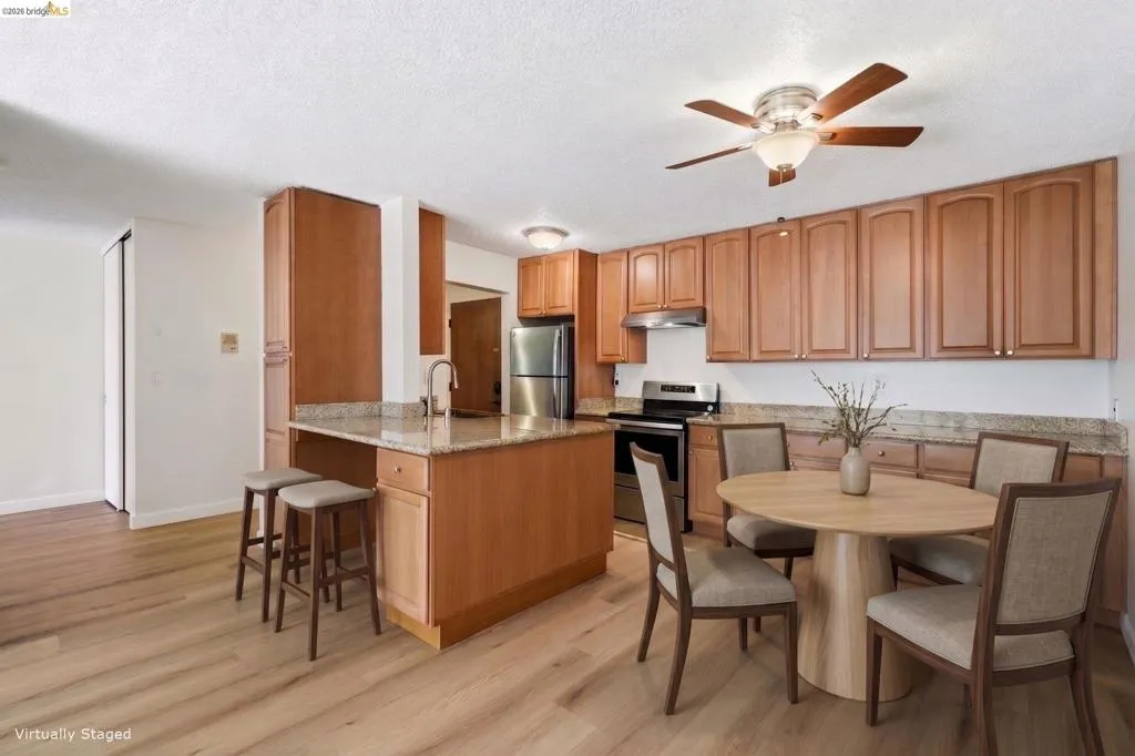 Kitchen and dining area featuring wood-finish flooring, light wood cabinetry, stone countertops, and stainless steel appliances