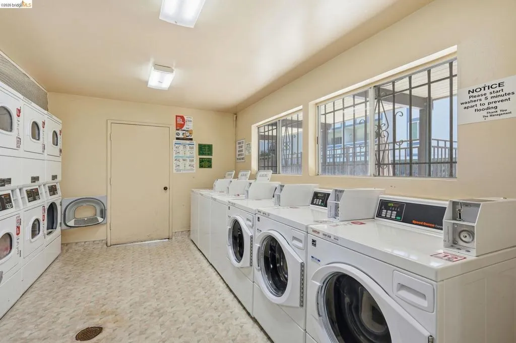 Community laundry room featuring multiple front-loading and top-loading washing machines, stacked dryers, and a durable tile-patterned floor
