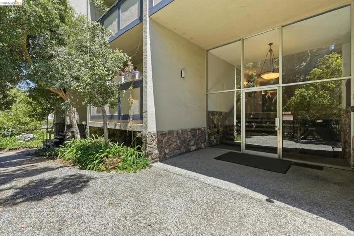 Building entrance featuring a floor-to-ceiling glass facade, stone-clad base, and an exposed aggregate concrete landing