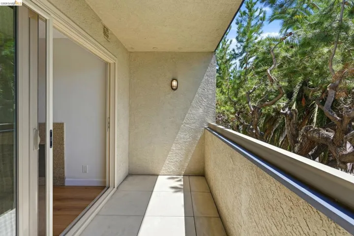 Private balcony featuring light-colored tile flooring, stucco walls, and a contemporary wall-mounted light fixture