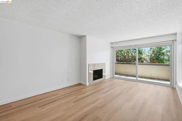 Spacious room featuring wood-finish flooring, a contemporary fireplace with a stone surround, and a large sliding glass door opening to a private balcony