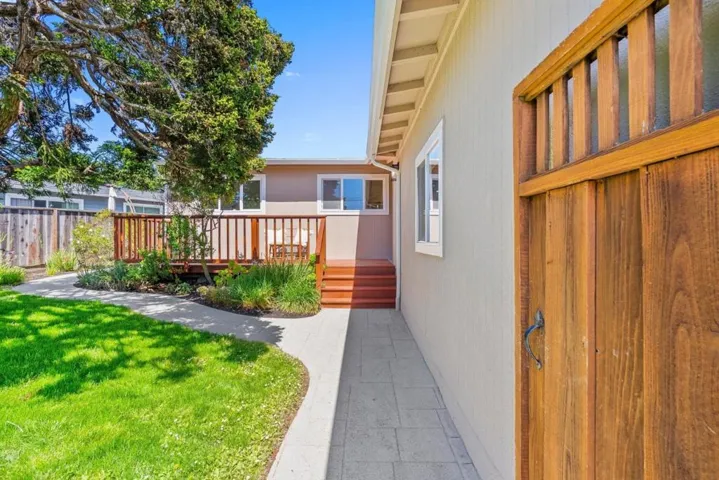 Privacy gate and fenced front yard with seasonal landscaping and a sunny entry deck
