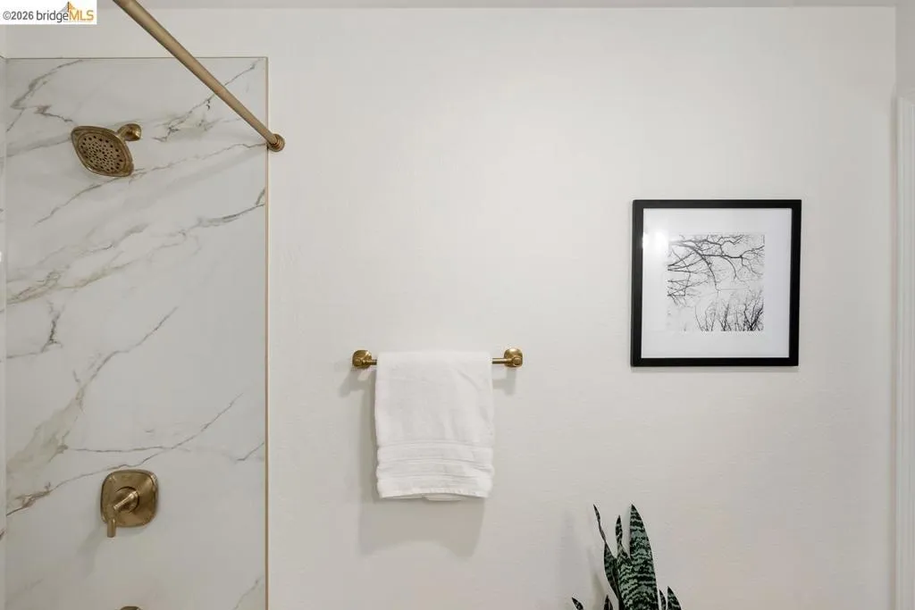 Shower with large-format marble-look wall tiling, featuring a gold-toned showerhead and control hardware Shower with large-format marble-look wall tiling, featuring a gold-toned showerhead and control hardware
