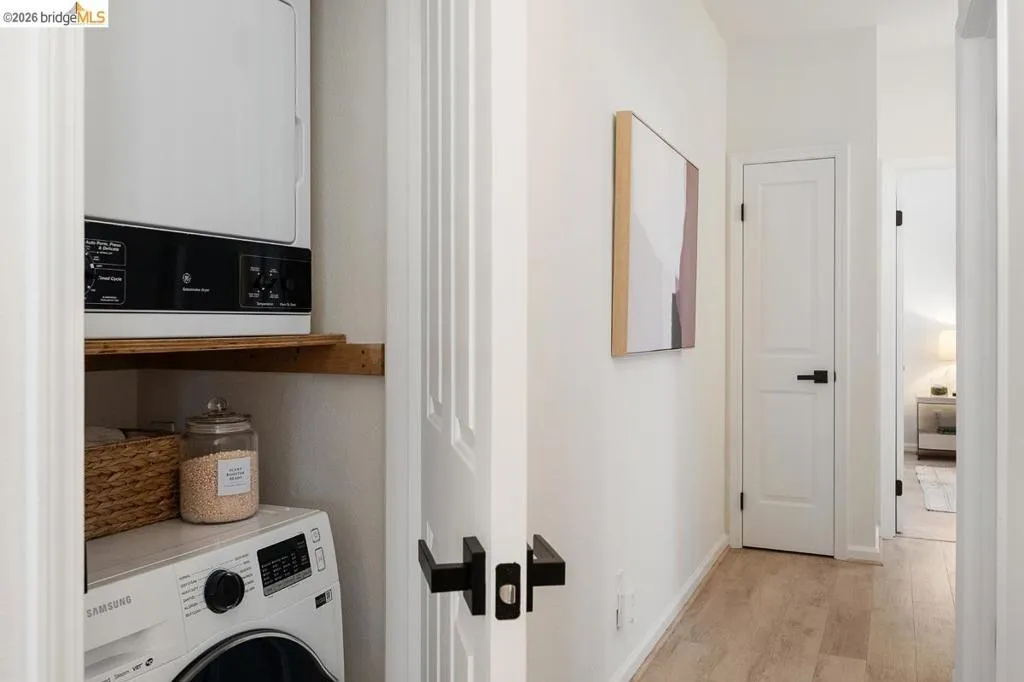 Laundry closet featuring a stacked washer and dryer unit, wood-finish shelving, and white paneled doors with matte black hardware Laundry closet featuring a stacked washer and dryer unit, wood-finish shelving, and white paneled doors with matte black hardware