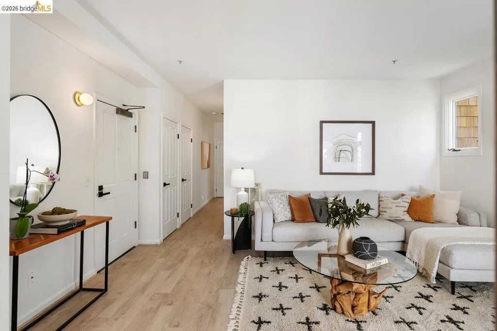 Bright living space featuring light wood-finish flooring, white walls, multiple interior doors with matte black hardware, and a window with wood siding visible Bright living space featuring light wood-finish flooring, white walls, multiple interior doors with matte black hardware, and a window with wood siding visible