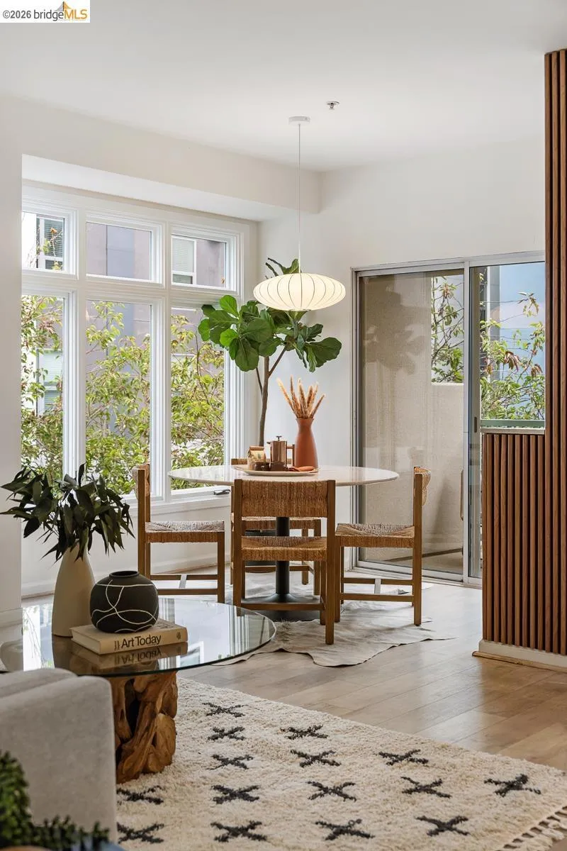 Open-concept living area featuring light wood-finish flooring, a large multi-pane window, and a sliding glass door to a private outdoor space Open-concept living area featuring light wood-finish flooring, a large multi-pane window, and a sliding glass door to a private outdoor space