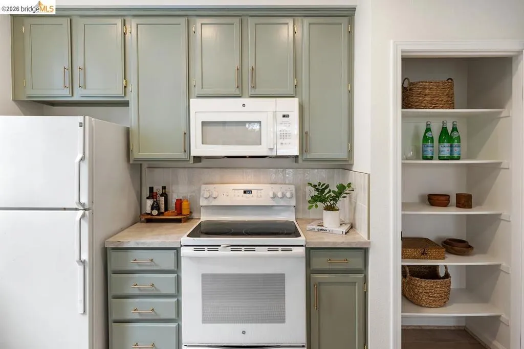 Kitchen featuring sage green cabinetry with gold-tone hardware, white appliances, and a light-toned countertop Kitchen featuring sage green cabinetry with gold-tone hardware, white appliances, and a light-toned countertop