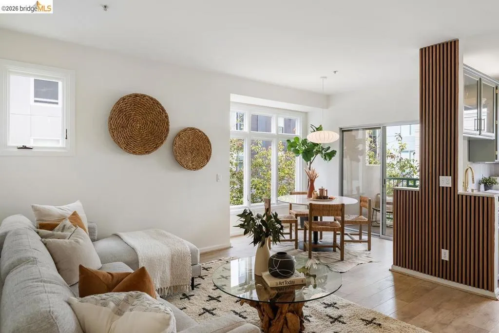 Open-concept living and dining area featuring light-toned wood-finish flooring, white walls, and a large window Open-concept living and dining area featuring light-toned wood-finish flooring, white walls, and a large window
