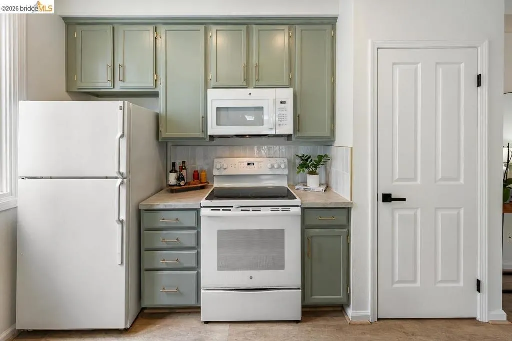 Kitchen area featuring green cabinetry, white appliances including a refrigerator and range with an over-the-range microwave, and a light-toned countertop Kitchen area featuring green cabinetry, white appliances including a refrigerator and range with an over-the-range microwave, and a light-toned countertop