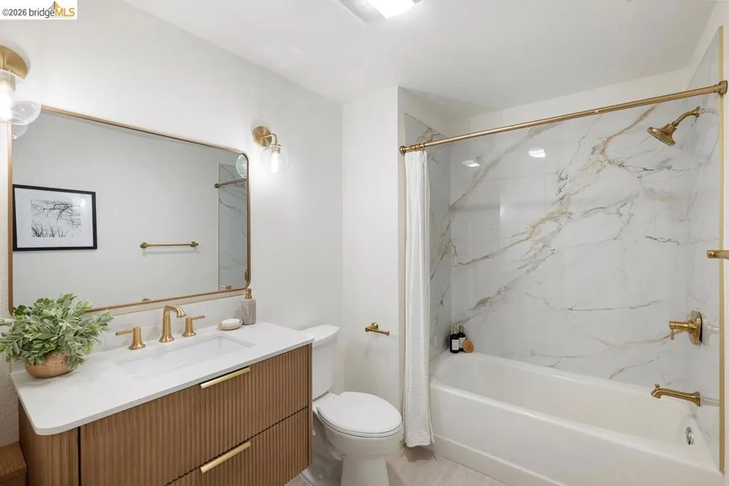 Bathroom featuring a white bathtub with a faux marble surround, gold-finish fixtures, and a coordinating gold-framed mirror Bathroom featuring a white bathtub with a faux marble surround, gold-finish fixtures, and a coordinating gold-framed mirror