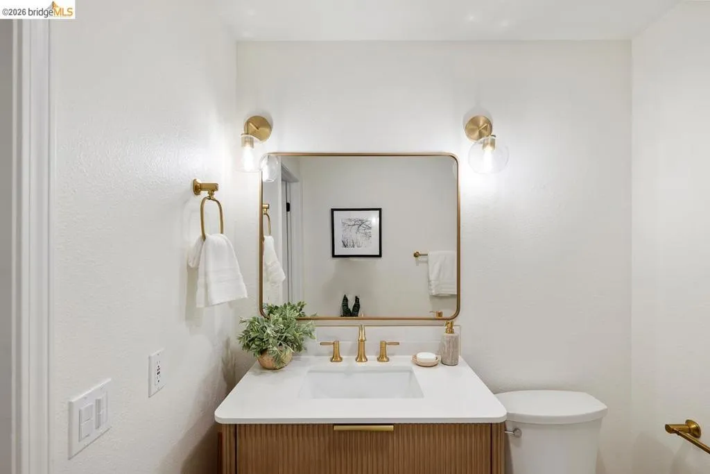Powder room featuring a wood-finish vanity with fluted detailing, a white countertop, and a rectangular undermount sink with a gold-tone faucet Powder room featuring a wood-finish vanity with fluted detailing, a white countertop, and a rectangular undermount sink with a gold-tone faucet