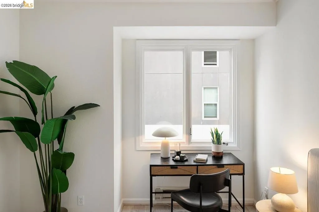Dedicated workspace featuring a window with white trim, light-toned walls, and wood-finish flooring Dedicated workspace featuring a window with white trim, light-toned walls, and wood-finish flooring