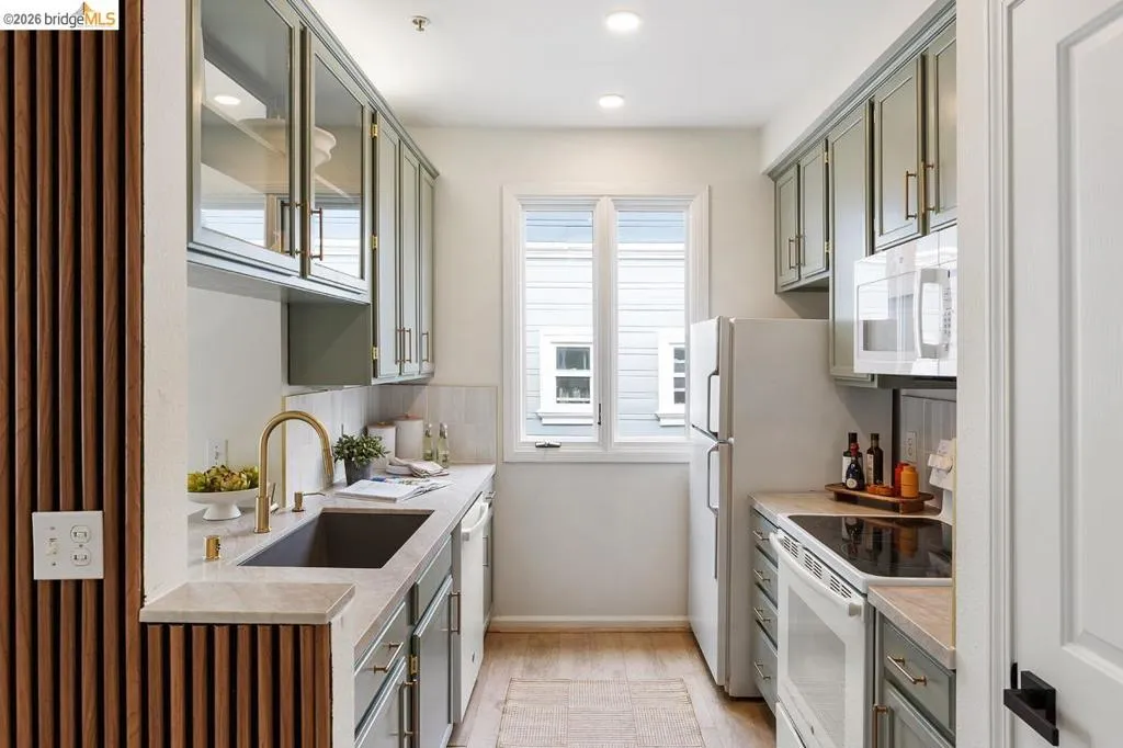 Galley kitchen featuring light green cabinetry, a single window, recessed lighting, and wood-finish flooring Galley kitchen featuring light green cabinetry, a single window, recessed lighting, and wood-finish flooring