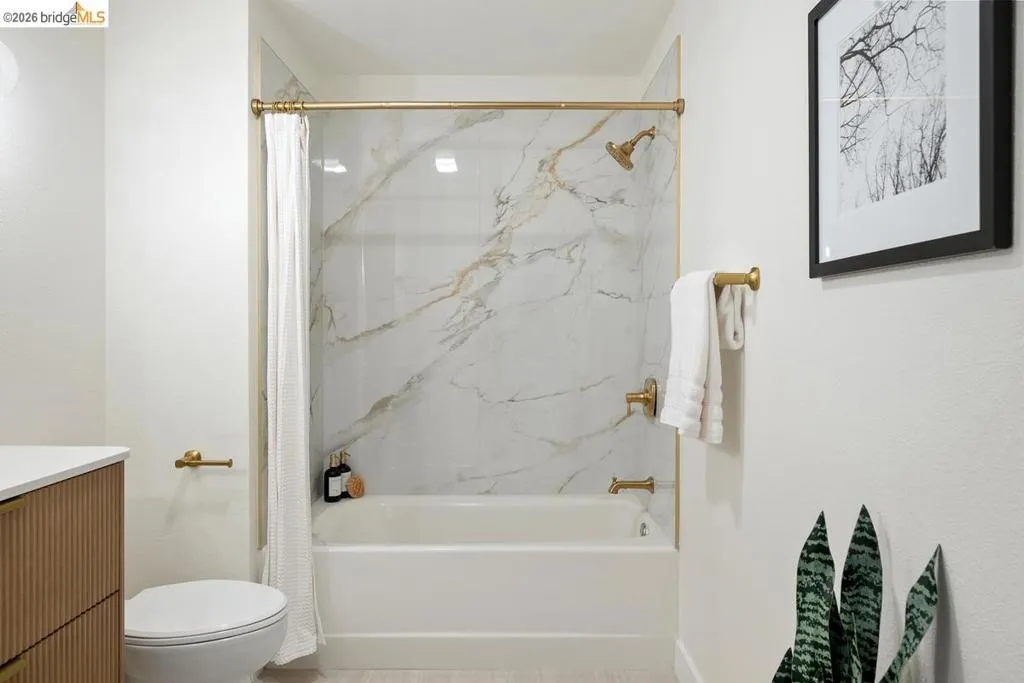 Bathroom featuring a built-in bathtub with shower, accented by white and gold veined wall panels Bathroom featuring a built-in bathtub with shower, accented by white and gold veined wall panels