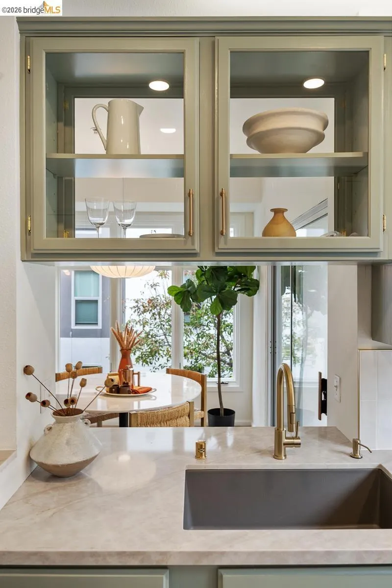 Kitchen featuring light green cabinetry with glass-front upper cabinets, under-cabinet lighting, and gold-tone hardware Kitchen featuring light green cabinetry with glass-front upper cabinets, under-cabinet lighting, and gold-tone hardware
