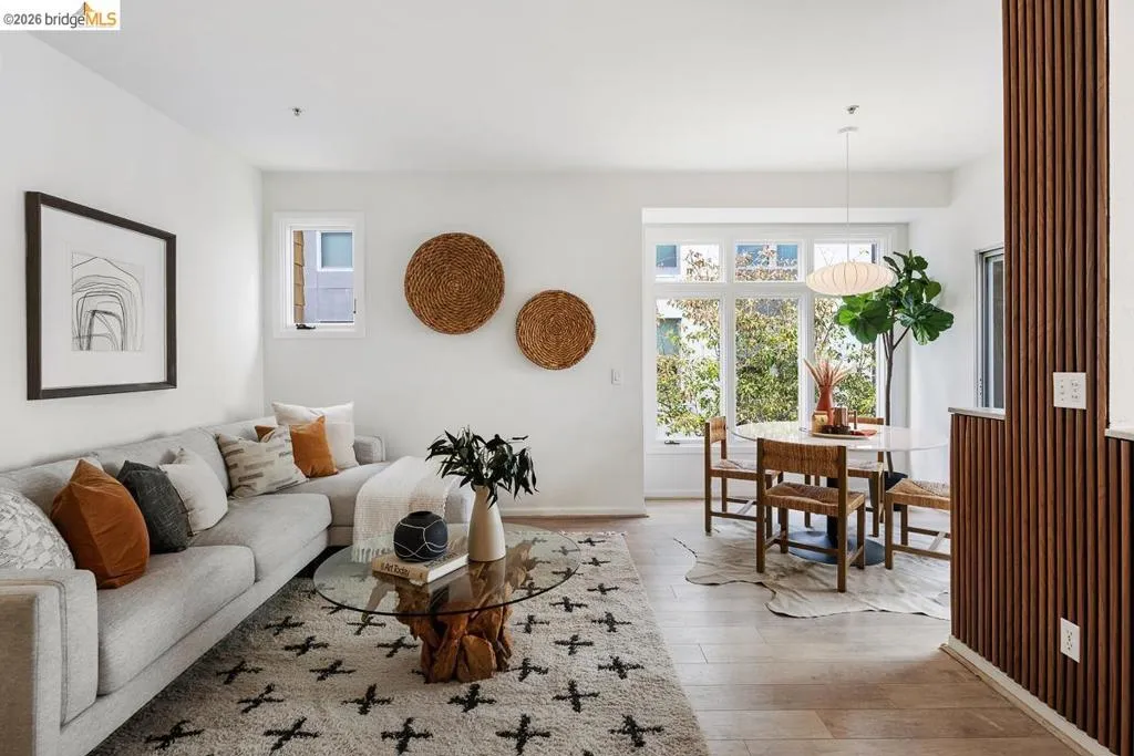 Open-concept living area featuring light wood-finish flooring, white walls, a large bay window, and a vertical wood slat wall accent Open-concept living area featuring light wood-finish flooring, white walls, a large bay window, and a vertical wood slat wall accent