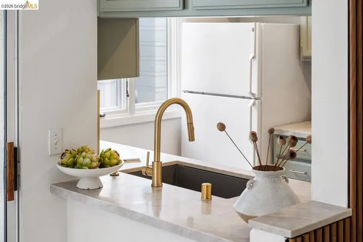 Kitchen pass-through featuring a deep-set sink with a brass-finish faucet, light-toned countertop, and light green cabinetry