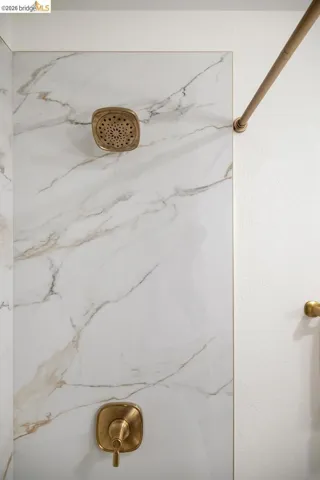 Shower area with large format veined wall tiles, a square-shaped shower head, and coordinating antique brass fixtures