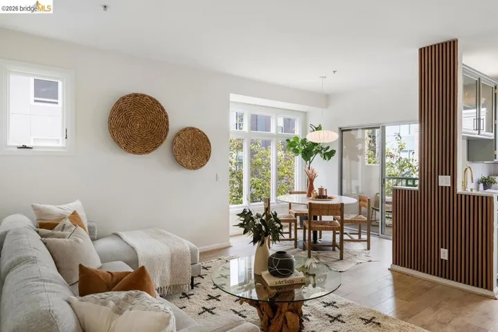 Open-concept living and dining area featuring light-toned wood-finish flooring, white walls, and a large window