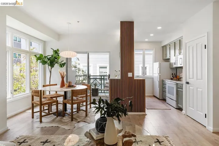Open-concept living area featuring wood-finish flooring, recessed lighting, a private balcony, and a kitchen with light green cabinetry and white appliances