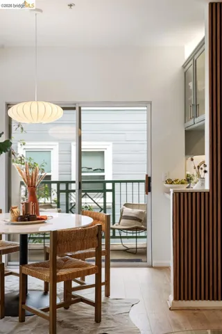 Dining area featuring wood-finish flooring, a white circular table, and a sliding glass door opening to a balcony with green metal railings
