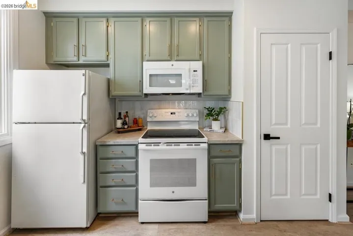 Kitchen area featuring green cabinetry, white appliances including a refrigerator and range with an over-the-range microwave, and a light-toned countertop
