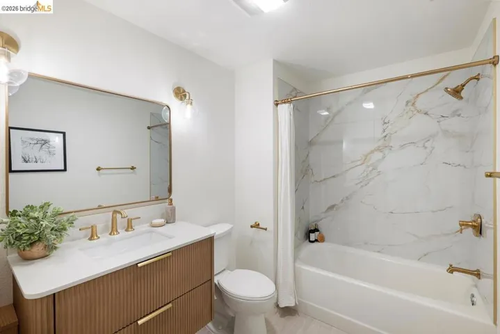 Bathroom featuring a white bathtub with a faux marble surround, gold-finish fixtures, and a coordinating gold-framed mirror