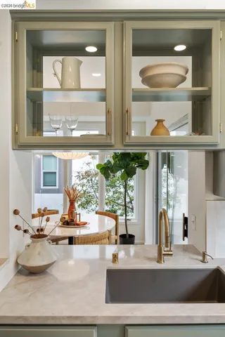 Kitchen featuring light green cabinetry with glass-front upper cabinets, under-cabinet lighting, and gold-tone hardware