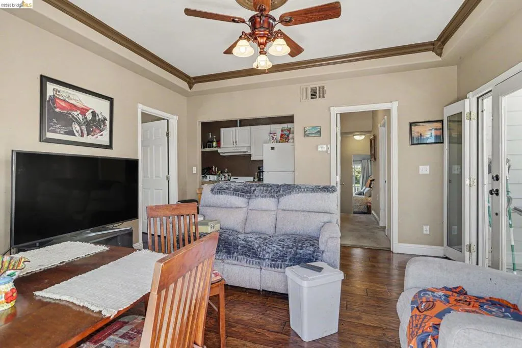 Living area with wood-finish flooring, crown molding, and a ceiling fan