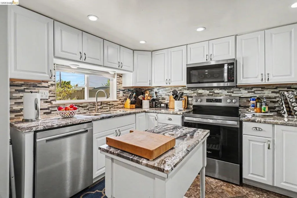 Modern kitchen featuring white cabinetry, stone-finish countertops, stainless steel appliances, a mosaic tile backsplash, and recessed lighting