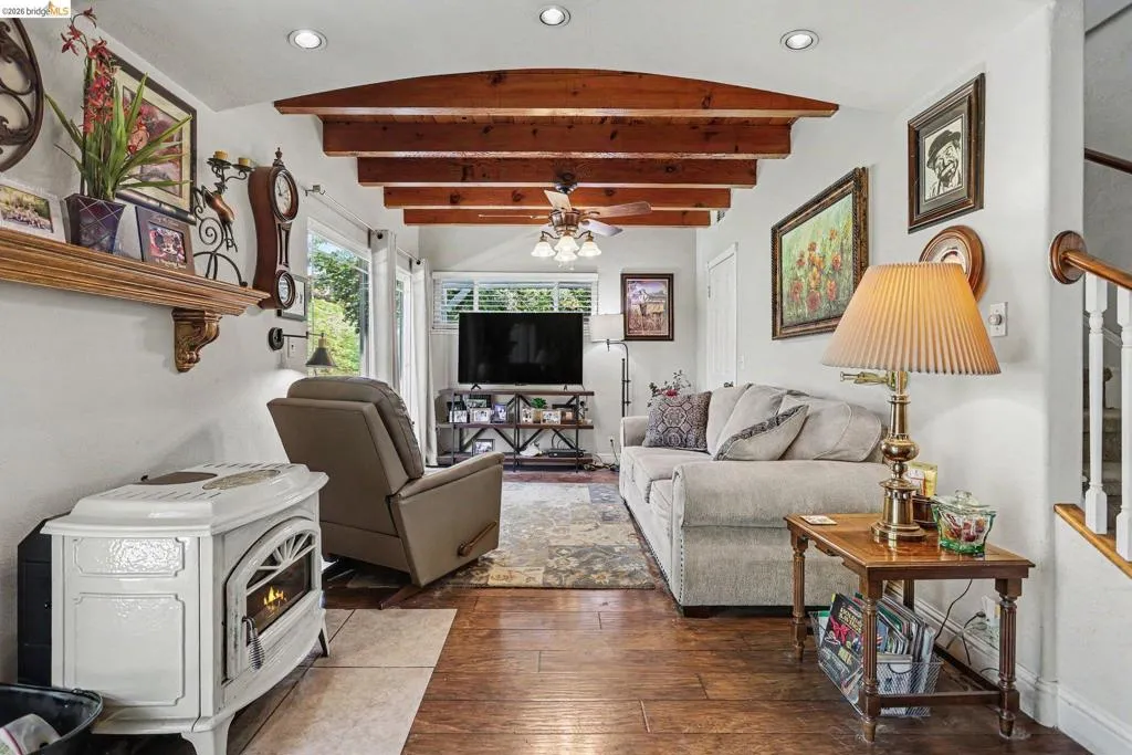 Living area featuring exposed wood ceiling beams, wood-finish flooring, a white free-standing fireplace, and recessed lighting