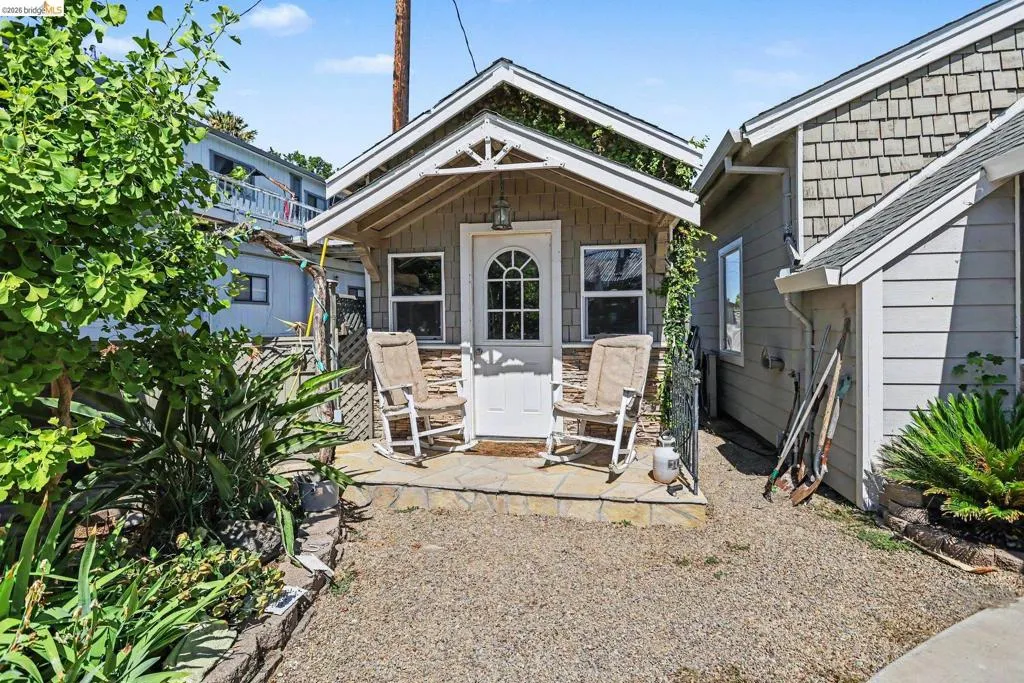 Charming cottage-style structure featuring a white arched door and two large windows