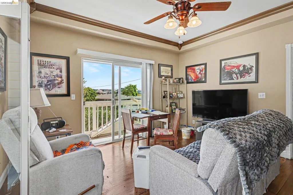 Living area featuring wood-finish flooring, a ceiling fan with integrated lighting, and a tray ceiling with crown molding
