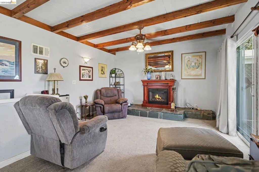 Vaulted ceiling with exposed wood beams, a fireplace with a wood mantel and stone hearth, and sliding glass doors