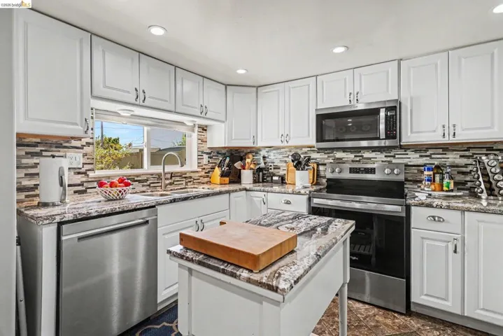Modern kitchen featuring white cabinetry, stone-finish countertops, stainless steel appliances, a mosaic tile backsplash, and recessed lighting