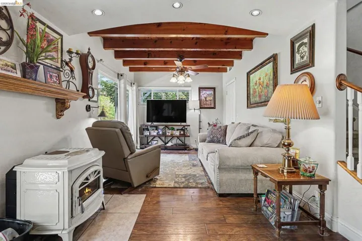 Living area featuring exposed wood ceiling beams, wood-finish flooring, a white free-standing fireplace, and recessed lighting