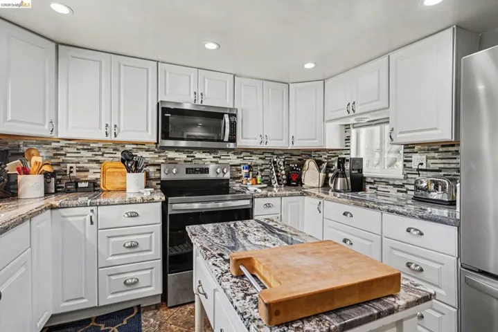 Kitchen featuring white shaker-style cabinetry, a multi-tone tile backsplash, built-in stainless steel microwave, and a freestanding stainless steel range with a flat cooktop