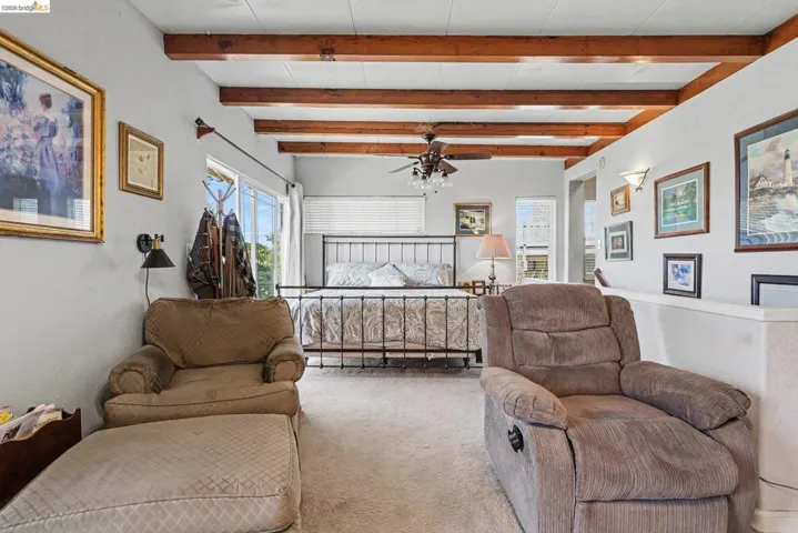 Spacious room featuring exposed wood ceiling beams, light-colored carpeting, and a ceiling fan with integrated lighting