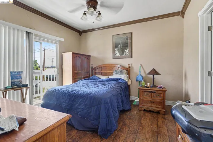 Room featuring wood-finish flooring, a ceiling fan with light fixture, sliding glass door with vertical blinds, and crown molding