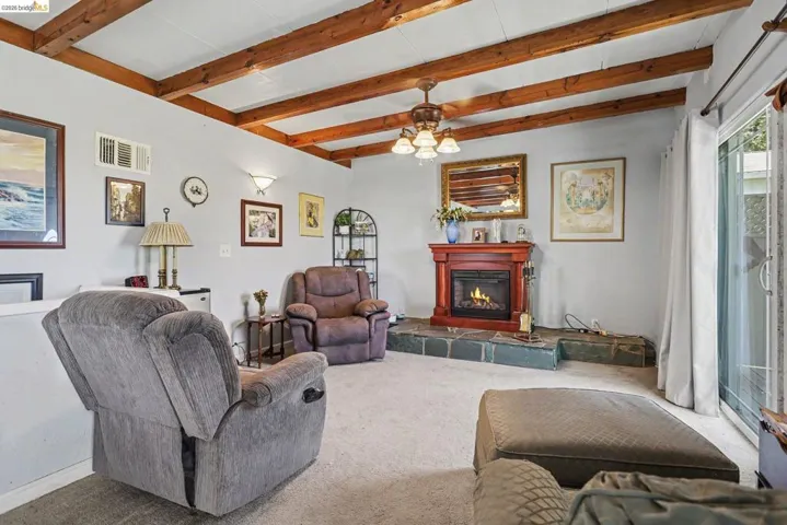 Vaulted ceiling with exposed wood beams, a fireplace with a wood mantel and stone hearth, and sliding glass doors