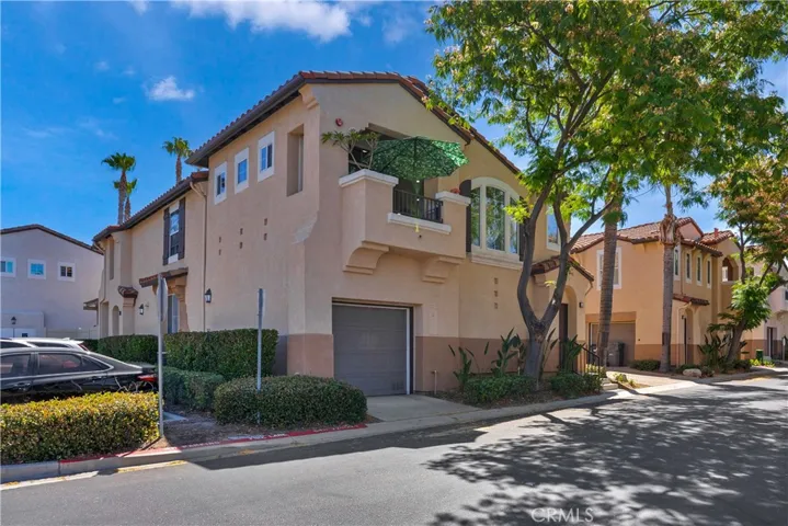 ADDITONAL EXTERIOR VIEW SHOWCASING THE HOME'S DESIRABLE CORNER LOCATION, PRIVATE BALCONY, MATURE SHADE TREE, AND MEDITERANEAN-STYLE ARCHITECTURE.