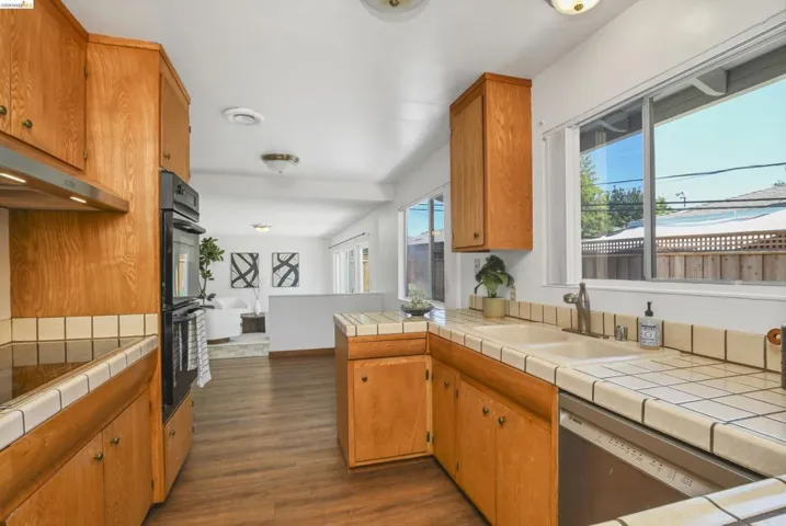 Kitchen featuring wood cabinetry, tile countertops, built-in double ovens, and a dual-basin sink