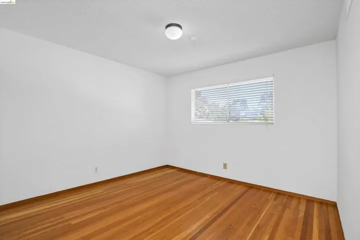 Bright interior space featuring wood-finish flooring, white walls, a large window with horizontal blinds, and a flush-mount ceiling light fixture