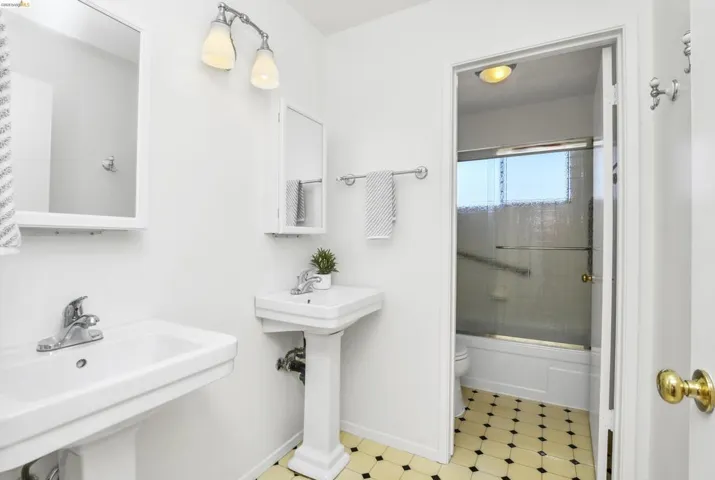 Bathroom featuring two pedestal sinks with chrome faucets, white framed wall mirrors, and a two-light vanity fixture