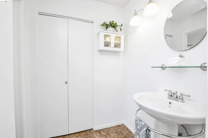 White pedestal sink with chrome fixtures, round wall mirror, and overhead vanity lighting